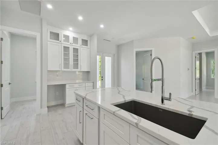 Kitchen featuring white cabinetry, light stone countertops, light hardwood / wood-style flooring, sink, and tasteful backsplash