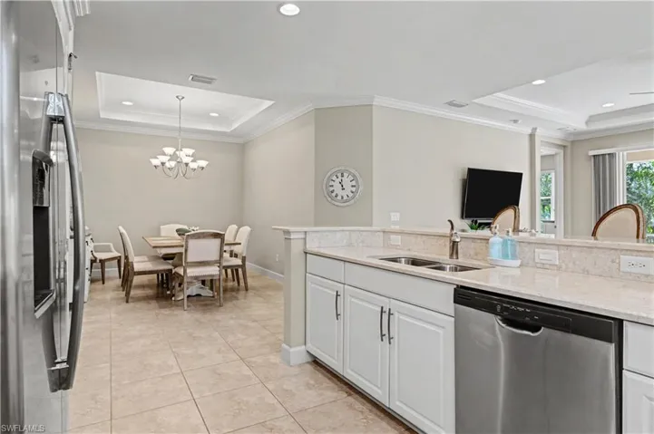 Kitchen with a tray ceiling, stainless steel appliances, light stone countertops, crown molding, and white cabinetry