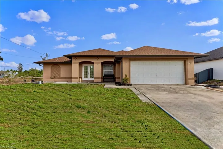 View of front facade featuring concrete driveway, stucco siding, french doors, a front yard, and a garage