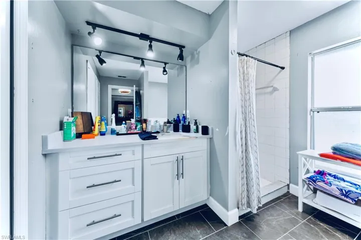 Bathroom featuring a stall shower, vanity, baseboards, and rail lighting