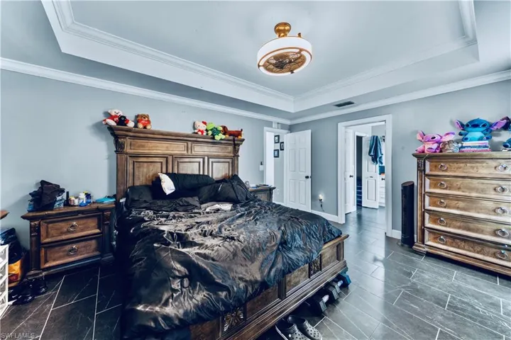 Bedroom featuring visible vents, baseboards, ornamental molding, and a raised ceiling