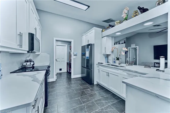 Kitchen with visible vents, black range with electric cooktop, freestanding refrigerator, white cabinetry, and light stone counters
