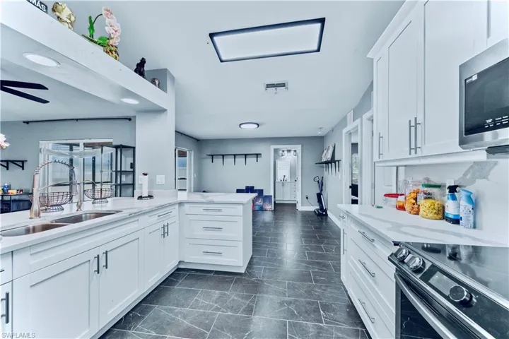 Kitchen featuring visible vents, range with electric cooktop, a sink, stainless steel microwave, and white cabinetry