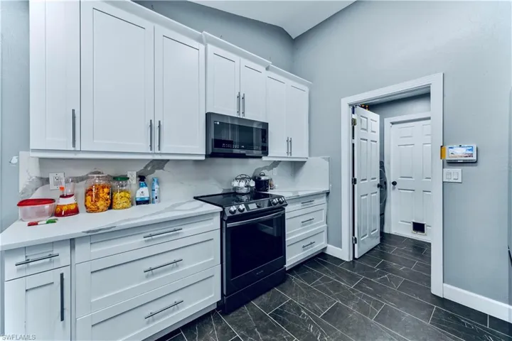 Kitchen with baseboards, white cabinetry, marble finish floor, and electric range