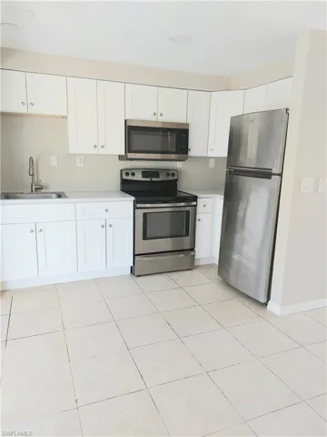 Kitchen with stainless steel appliances, a sink, white cabinetry, light countertops, and light tile patterned floors
