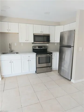 Kitchen featuring stainless steel appliances, a sink, light countertops, and white cabinetry
