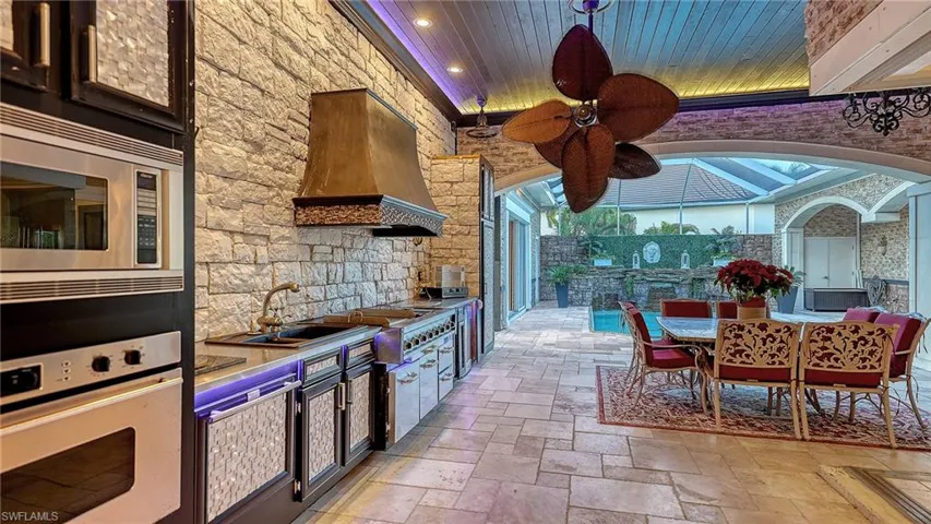 Kitchen with stainless steel appliances, premium range hood, stone tile floors, recessed lighting, and arched walkways