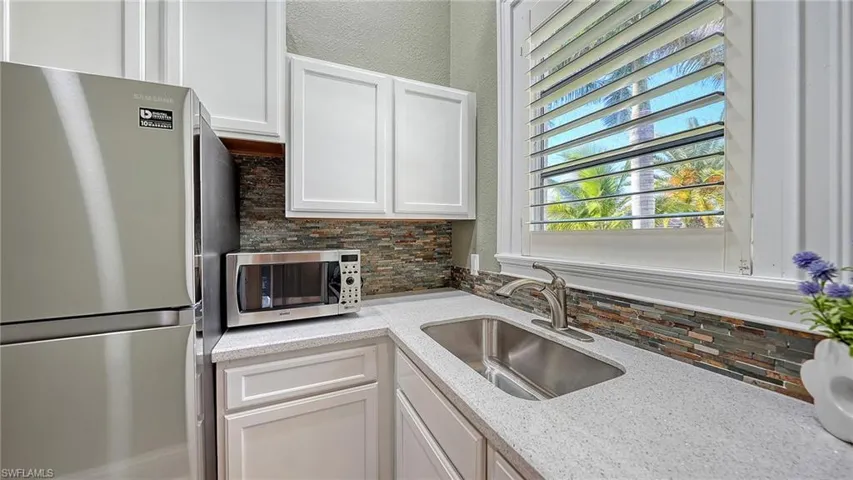 Kitchen featuring stainless steel appliances, tasteful backsplash, white cabinetry, and light stone countertops