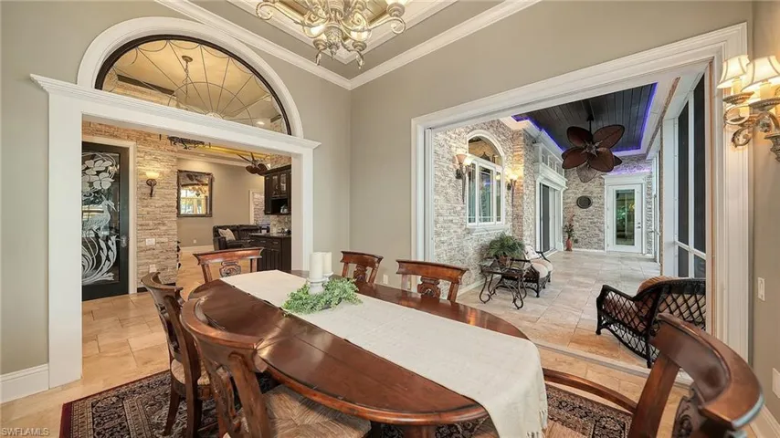 Dining area with crown molding, healthy amount of natural light, a chandelier, and stone tile floors