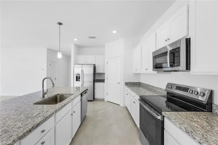 Kitchen with stainless steel appliances, hanging light fixtures, white cabinetry, dark stone countertops, and an island with sink