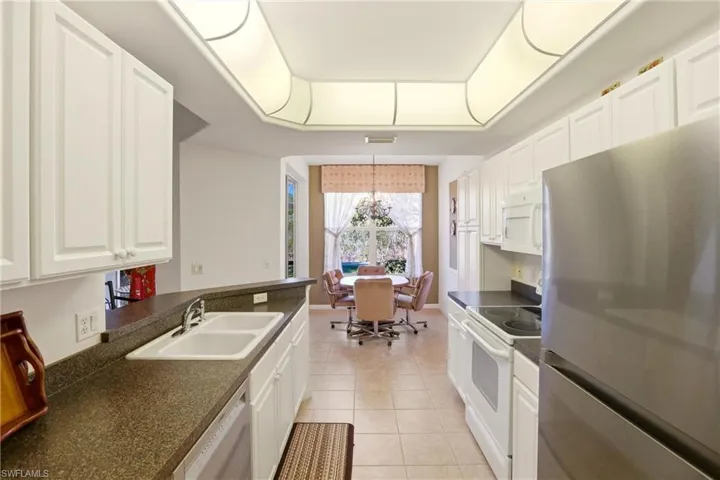 Kitchen featuring appliances with stainless steel finishes, dark countertops, white cabinets, light tile patterned flooring, and a raised ceiling