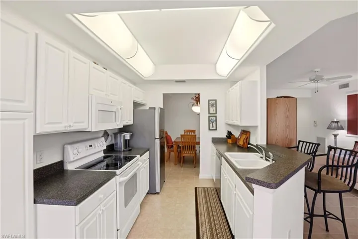 Kitchen featuring white appliances, dark countertops, white cabinets, and a breakfast bar