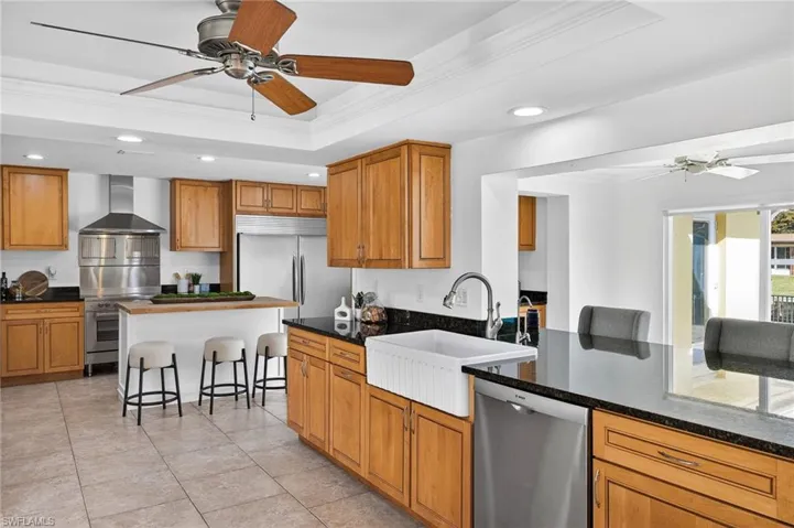 Kitchen with a ceiling fan, a breakfast bar area, recessed lighting, dark stone countertops, and wood finish cabinets