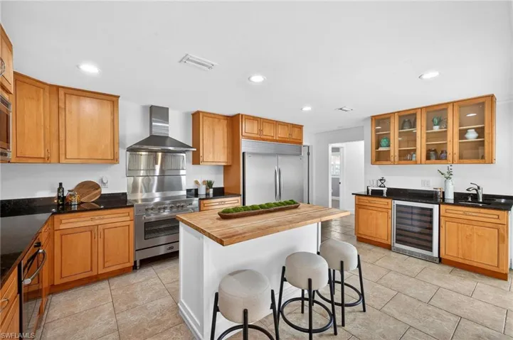Kitchen featuring a breakfast bar area, wine cooler, high quality appliances, dark stone counters, and wood finish cabinetry