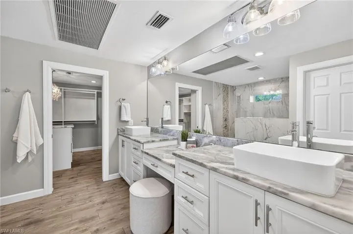 Full bath with a spacious closet, two vanities, recessed lighting, light wood-type flooring, and a marble finish shower