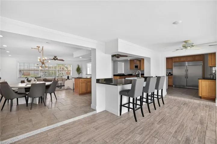 Kitchen featuring a ceiling fan, built in appliances, wood finish cabinetry, a breakfast bar, and ornamental molding