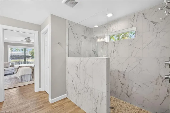 Ensuite bathroom featuring a marble finish shower, plenty of natural light, light wood finished floors, and a ceiling fan