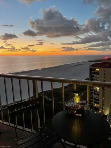 Balcony at dusk with a water view and a view of the beach