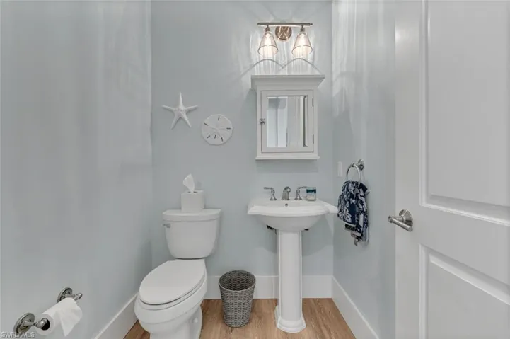 Half bathroom featuring toilet, a sink, baseboards, and wood finished floors