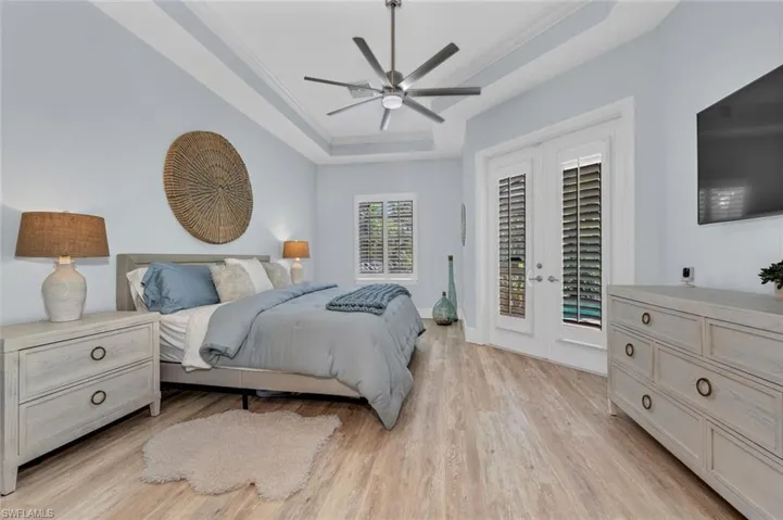 Bedroom featuring light wood-style flooring, crown molding, access to exterior, a tray ceiling, and french doors