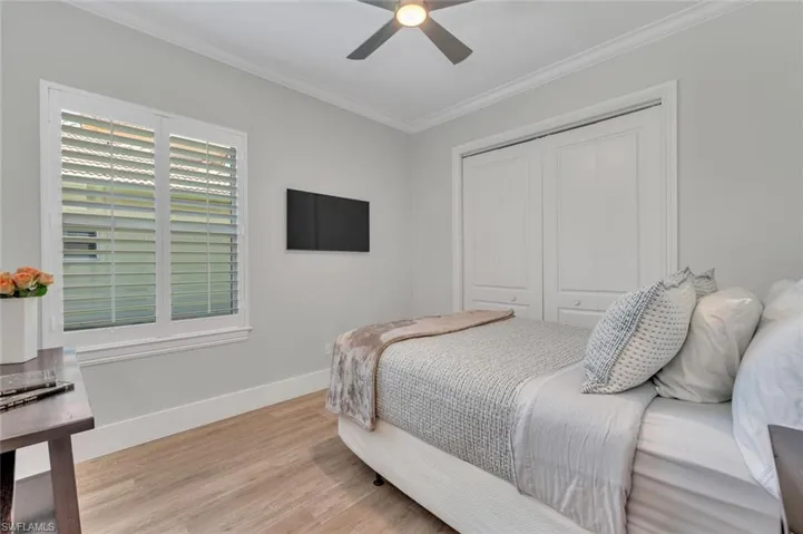 Bedroom with a closet, a ceiling fan, wood finished floors, baseboards, and ornamental molding