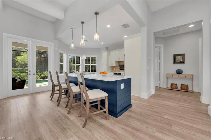 Kitchen with light countertops, light wood finished floors, decorative light fixtures, french doors, and a kitchen breakfast bar