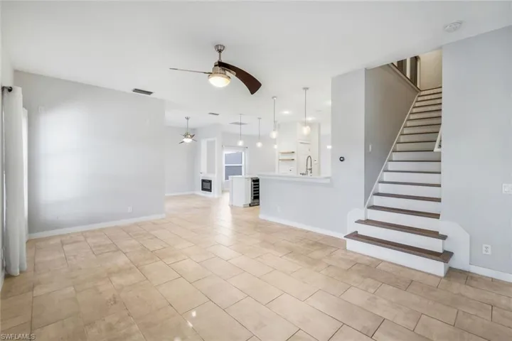 Unfurnished living room featuring visible vents, baseboards, ceiling fan, stairs, and a sink