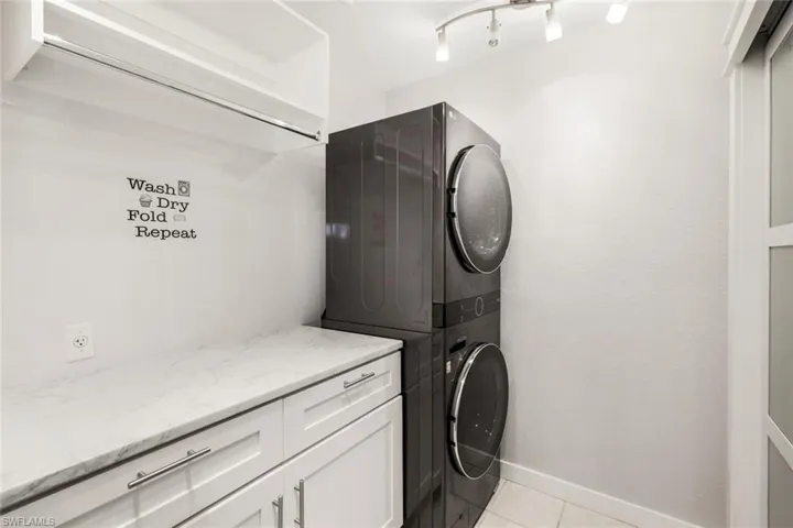 Laundry area with stacked washer and dryer, cabinet space, rail lighting, light tile patterned floors, and baseboards