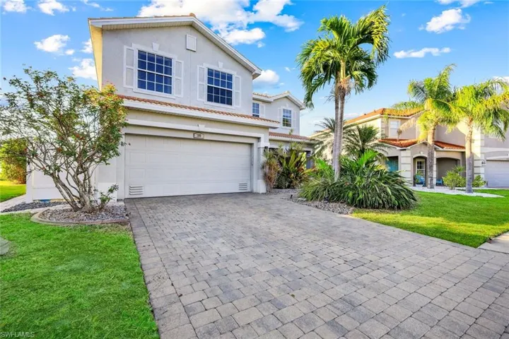 Traditional-style home with a garage, decorative driveway, a front lawn, and stucco siding