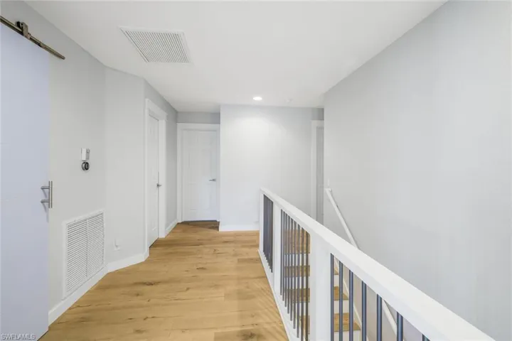 Hall featuring a barn door, an upstairs landing, light wood-style floors, and visible vents