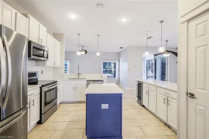 Kitchen featuring wine cooler, light countertops, a peninsula, stainless steel appliances, and a sink