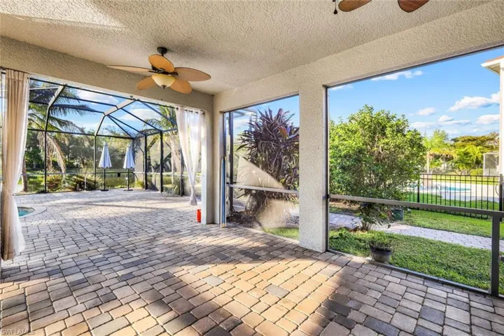 View of patio with glass enclosure, a ceiling fan, and fence