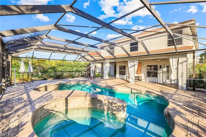 View of pool featuring a patio area, glass enclosure, and a pool with connected hot tub