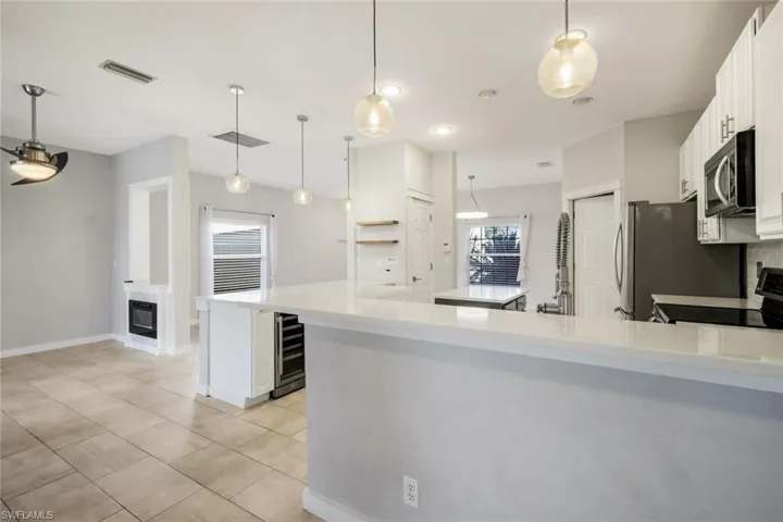 Kitchen with visible vents, electric stove, stainless steel microwave, white cabinetry, and wine cooler