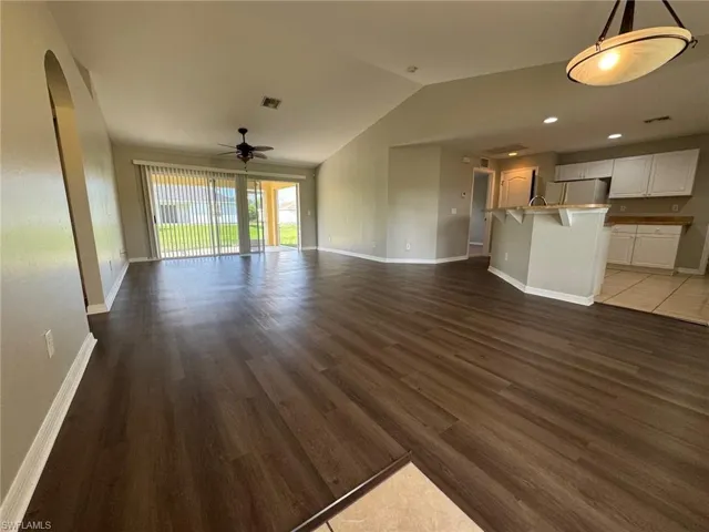 Unfurnished living room with dark wood finished floors, lofted ceiling, ceiling fan, and arched walkways