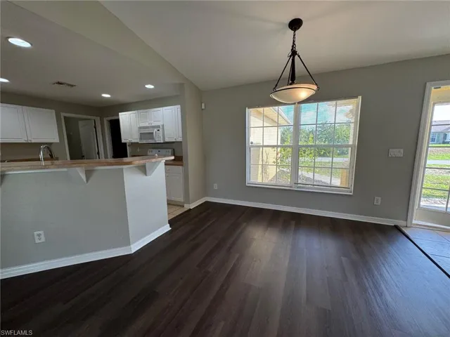 Kitchen featuring a kitchen breakfast bar, white cabinetry, hanging light fixtures, dark wood-type flooring, and light countertops