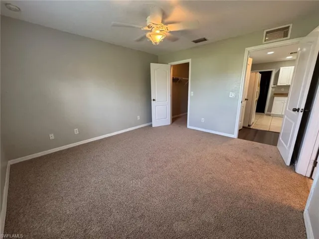 Unfurnished bedroom featuring dark carpet, a walk in closet, ceiling fan, and freestanding refrigerator