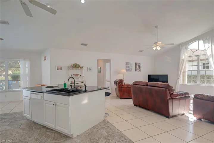 Kitchen featuring ceiling fan, open floor plan, white cabinets, and lofted ceiling