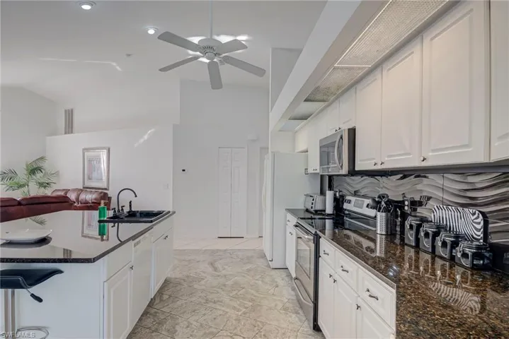 Kitchen featuring open floor plan, stainless steel appliances, dark stone counters, white cabinets, and vaulted ceiling