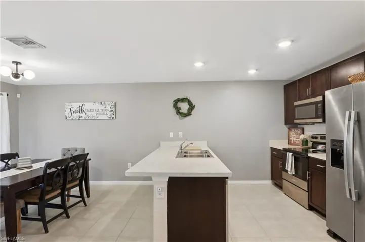 Kitchen with appliances with stainless steel finishes, a peninsula, light countertops, dark brown cabinets, and light tile patterned floors
