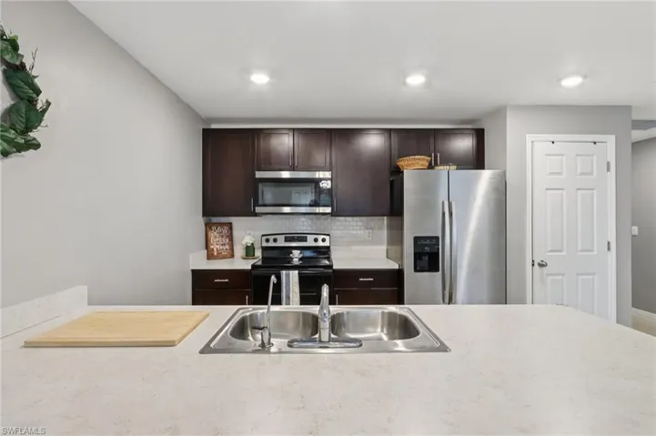 Kitchen featuring backsplash, stainless steel appliances, dark brown cabinets, and light countertops