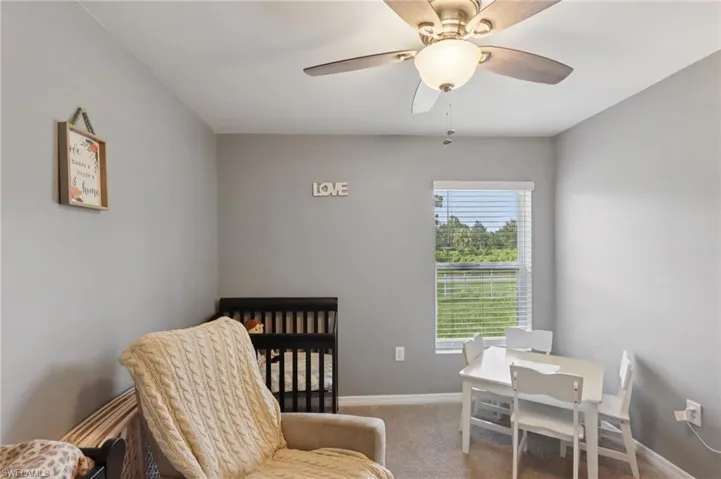 Carpeted bedroom with a ceiling fan and a crib