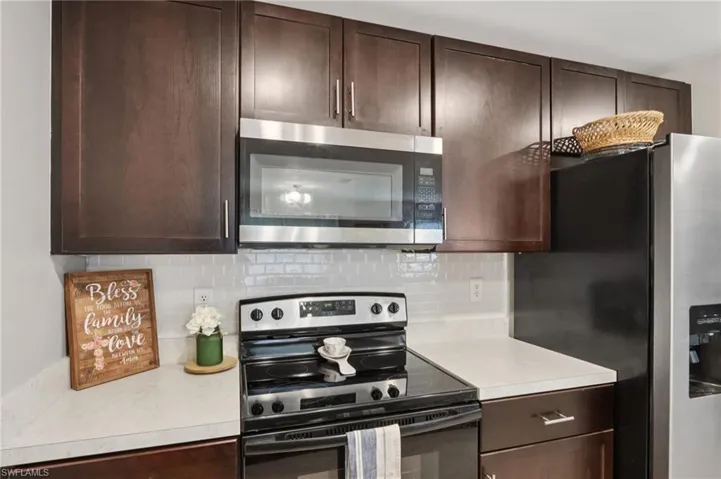 Kitchen with stainless steel appliances, light countertops, backsplash, and dark brown cabinets