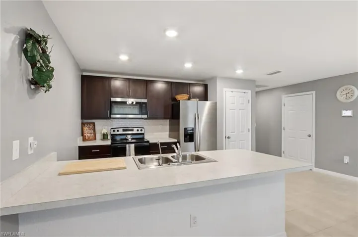 Kitchen with decorative backsplash, appliances with stainless steel finishes, dark brown cabinetry, light countertops, and recessed lighting