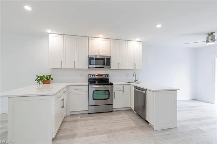 Kitchen featuring appliances with stainless steel finishes, white cabinetry, sink, kitchen peninsula, and ceiling fan