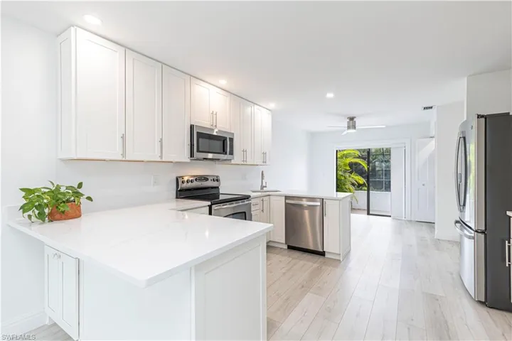 Kitchen featuring light stone countertops, white cabinetry, appliances with stainless steel finishes, and kitchen peninsula