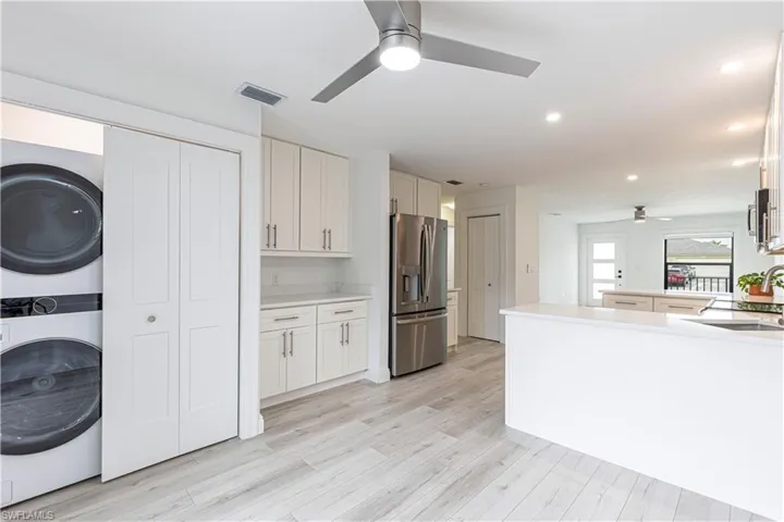 Kitchen with white cabinetry, stacked washer / drying machine, light hardwood / wood-style floors, stainless steel appliances, and sink