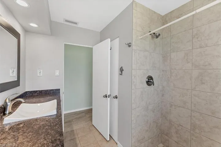 Bathroom featuring tiled shower, light tile patterned floors, and vanity