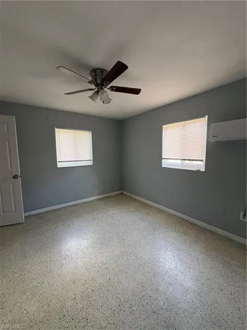 Empty room with dark speckled floor, ceiling fan, and a wall mounted mini split
