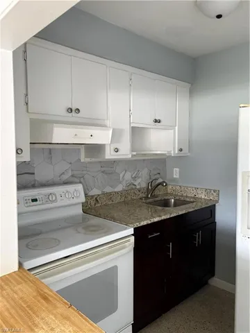 Dual tone kitchen with white range with electric cooktop, two tone cabinetry, backsplash, extractor fan, and dark aggregate flooring